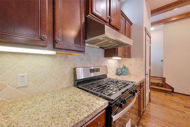 kitchen featuring light stone counters, decorative backsplash, light wood-style flooring, under cabinet range hood, and gas stove