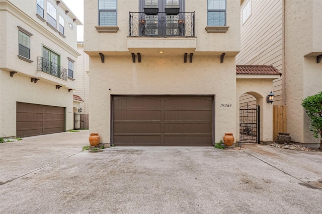 exterior space with stucco siding, driveway, a balcony, and an attached garage