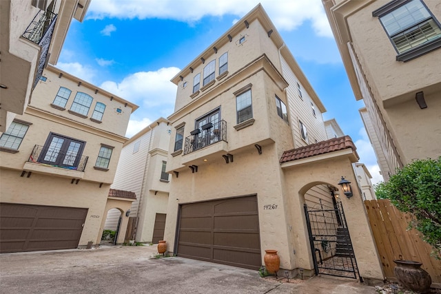 view of front facade featuring fence, a tile roof, a gate, an attached garage, and stucco siding
