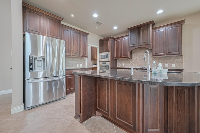 kitchen featuring dark stone counters, a sink, stainless steel appliances, light tile patterned floors, and visible vents