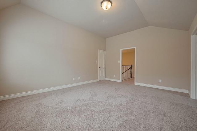 spare room featuring vaulted ceiling, light colored carpet, and baseboards