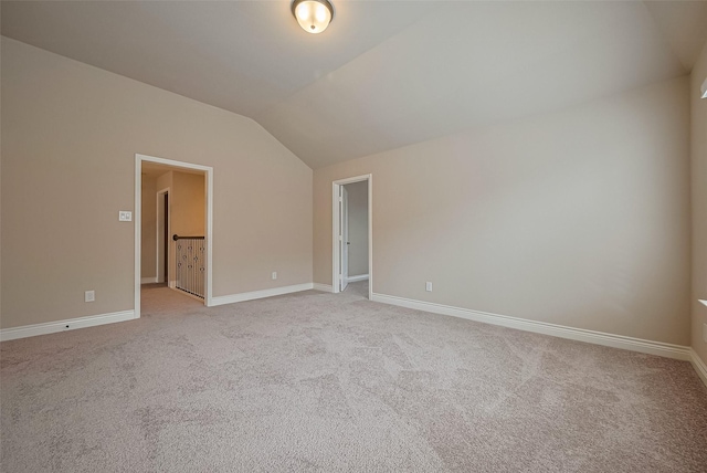 empty room with light colored carpet, vaulted ceiling, and baseboards