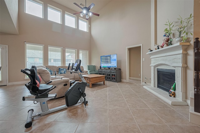 living area with light tile patterned floors, a high end fireplace, baseboards, a ceiling fan, and a towering ceiling