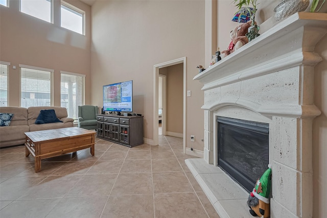 living room featuring light tile patterned floors, a glass covered fireplace, baseboards, and a high ceiling