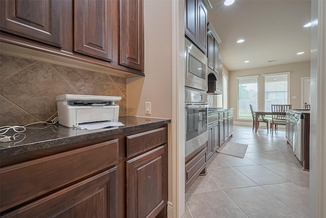 kitchen featuring recessed lighting, dark stone counters, stainless steel appliances, light tile patterned floors, and backsplash