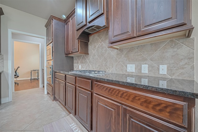 kitchen featuring dark stone counters, decorative backsplash, stainless steel appliances, baseboards, and light tile patterned flooring