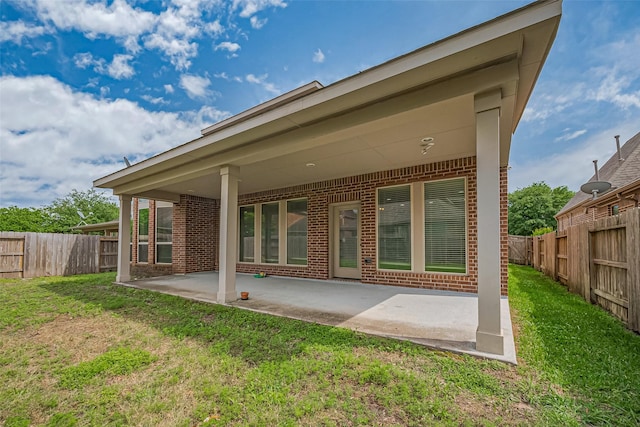 rear view of property featuring a yard, a patio area, brick siding, and a fenced backyard