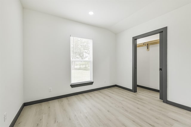 unfurnished bedroom with light wood finished floors, vaulted ceiling, and baseboards