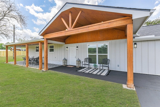 back of house with a lawn, fence, board and batten siding, and a patio area