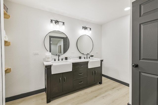 bathroom with baseboards, wood finished floors, double vanity, and a sink