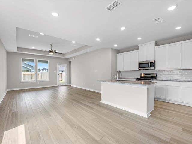 21703 White Bellflower Ln, Cypress, TX 77433 - kitchen with stainless steel appliances, decorative backsplash, a tray ceiling, light stone counters, and a kitchen island with sink