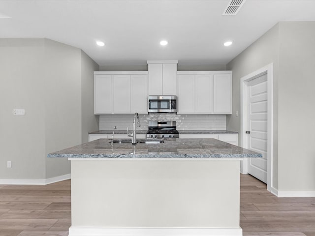 21703 White Bellflower Ln, Cypress, TX 77433 - kitchen featuring appliances with stainless steel finishes, light wood-style flooring, tasteful backsplash, an island with sink, and white cabinetry