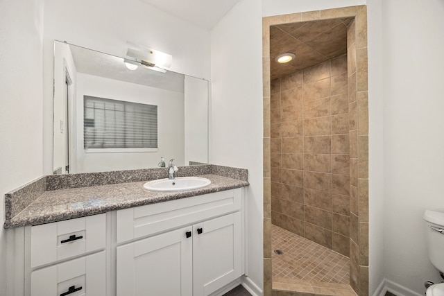 bathroom with toilet, a tile shower, and vanity