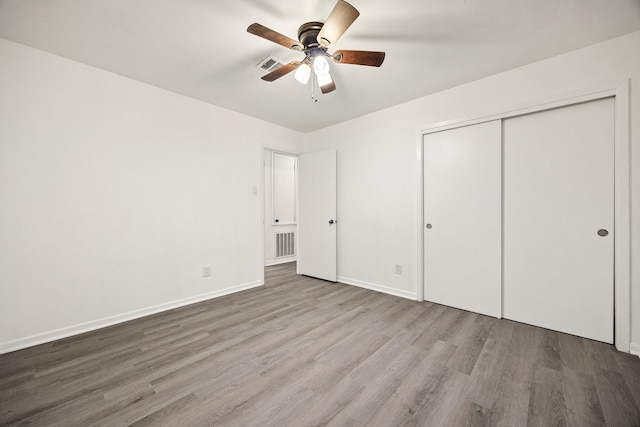 unfurnished bedroom featuring a closet, a ceiling fan, visible vents, baseboards, and wood finished floors