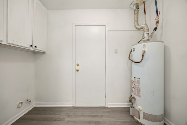 clothes washing area featuring water heater, wood finished floors, cabinet space, and baseboards