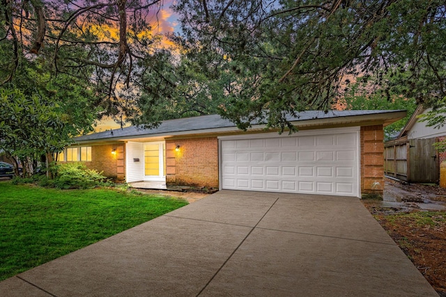 view of front of property featuring a garage, a lawn, driveway, brick siding, and fence
