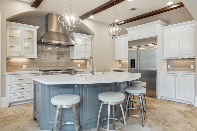 kitchen with visible vents, decorative backsplash, wall chimney range hood, built in refrigerator, and a sink