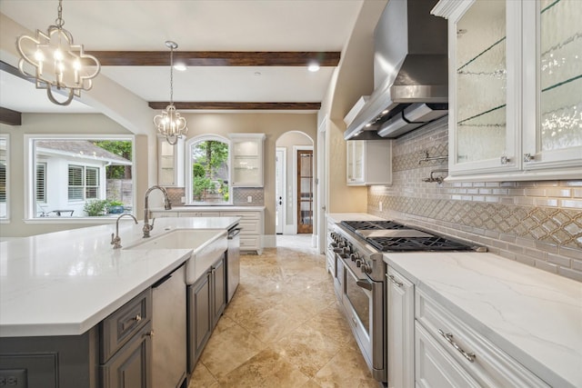 kitchen with beam ceiling, wall chimney range hood, a sink, appliances with stainless steel finishes, and a notable chandelier