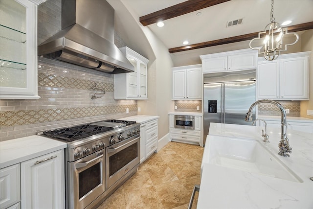 kitchen featuring built in appliances, glass insert cabinets, wall chimney range hood, tasteful backsplash, and a sink