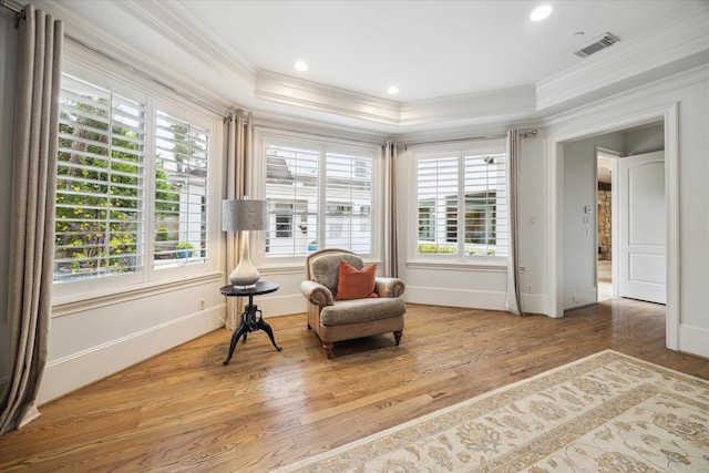 sitting room featuring crown molding, a raised ceiling, wood finished floors, and a healthy amount of sunlight