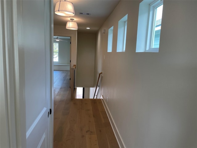 hall featuring wood-type flooring, an upstairs landing, visible vents, and baseboards