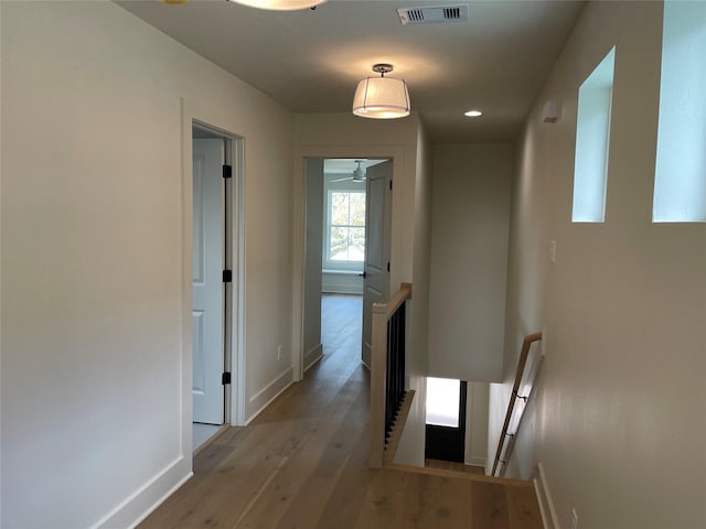hallway with baseboards, visible vents, wood finished floors, and an upstairs landing