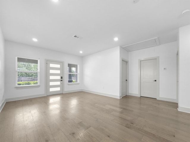 unfurnished living room with attic access, visible vents, wood finished floors, and plenty of natural light