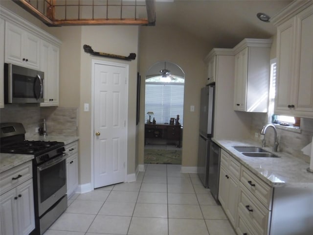 kitchen featuring white cabinetry, a sink, appliances with stainless steel finishes, light tile patterned flooring, and backsplash