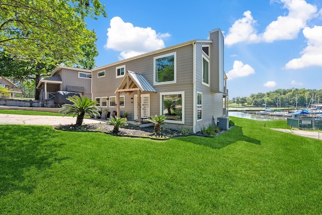 rear view of house featuring cooling unit, a water view, a yard, and a chimney