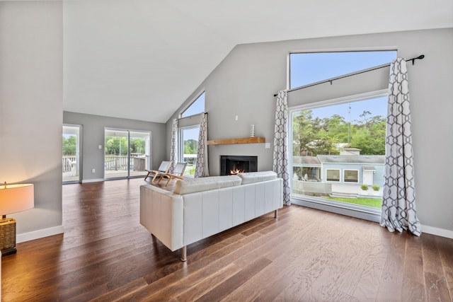 living area with baseboards, high vaulted ceiling, wood finished floors, and a lit fireplace