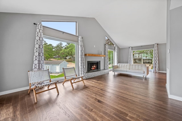 living area with baseboards, high vaulted ceiling, wood finished floors, and a lit fireplace
