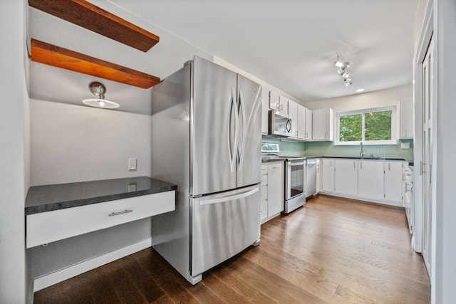 kitchen with wood finished floors, appliances with stainless steel finishes, white cabinets, dark countertops, and a sink