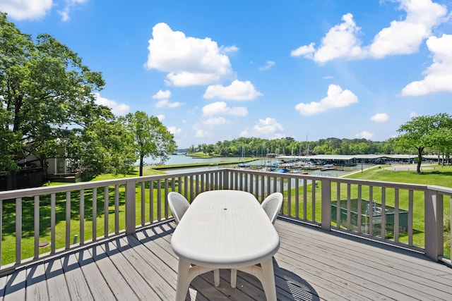 deck featuring outdoor dining space, a water view, and a lawn