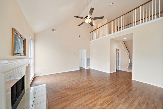 unfurnished living room featuring visible vents, a tile fireplace, a ceiling fan, high vaulted ceiling, and stairs