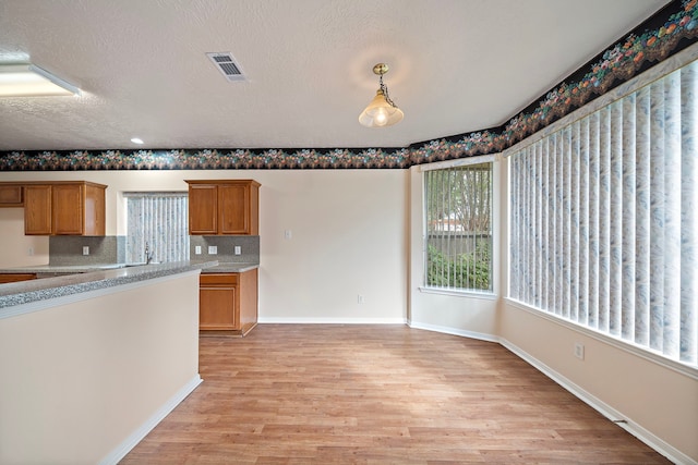 kitchen with light wood finished floors, brown cabinetry, tasteful backsplash, visible vents, and baseboards