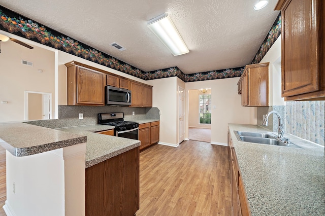 kitchen with light wood finished floors, a sink, visible vents, a peninsula, and appliances with stainless steel finishes