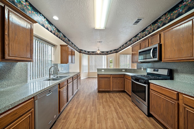 kitchen with stainless steel appliances, light wood-style floors, a textured ceiling, a sink, and a peninsula