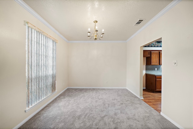 spare room with crown molding, visible vents, baseboards, an inviting chandelier, and light carpet