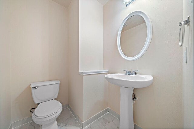 half bath featuring toilet, marble finish floor, and baseboards