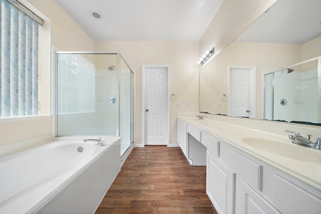 bathroom with a shower stall, a sink, double vanity, a bath, and wood finished floors