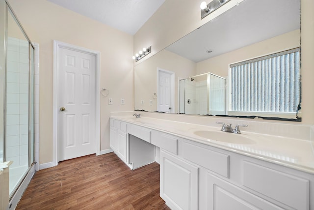 bathroom with double vanity, a sink, a shower stall, and wood finished floors