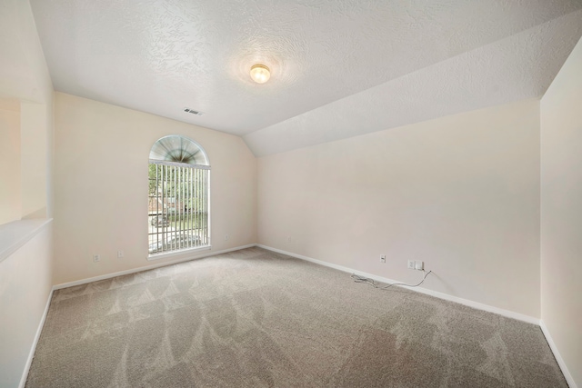 empty room featuring visible vents, a textured ceiling, lofted ceiling, and carpet