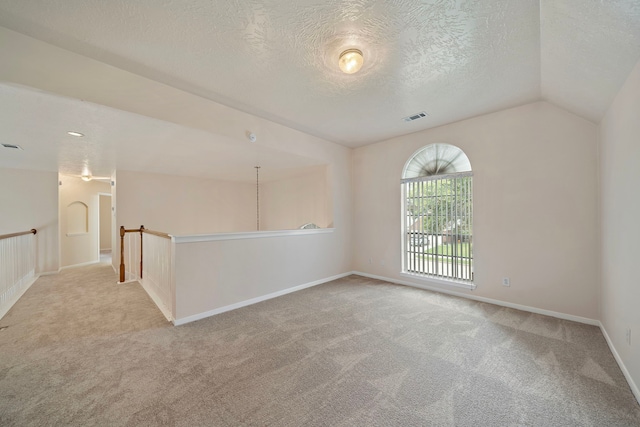 carpeted spare room with a textured ceiling, visible vents, vaulted ceiling, and baseboards