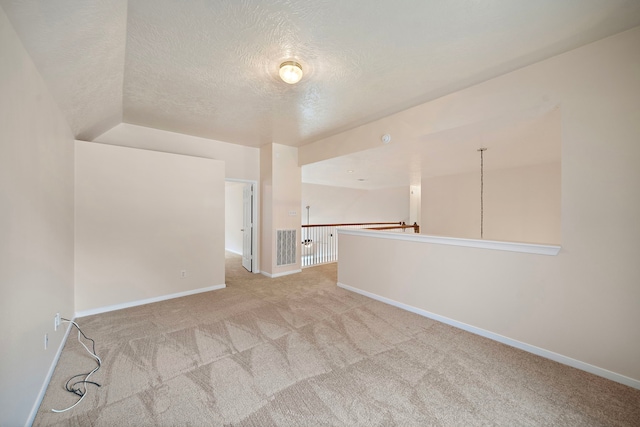 spare room featuring a textured ceiling, light colored carpet, and baseboards