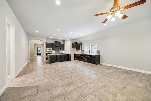 kitchen featuring stainless steel appliances, tasteful backsplash, light countertops, arched walkways, and open floor plan
