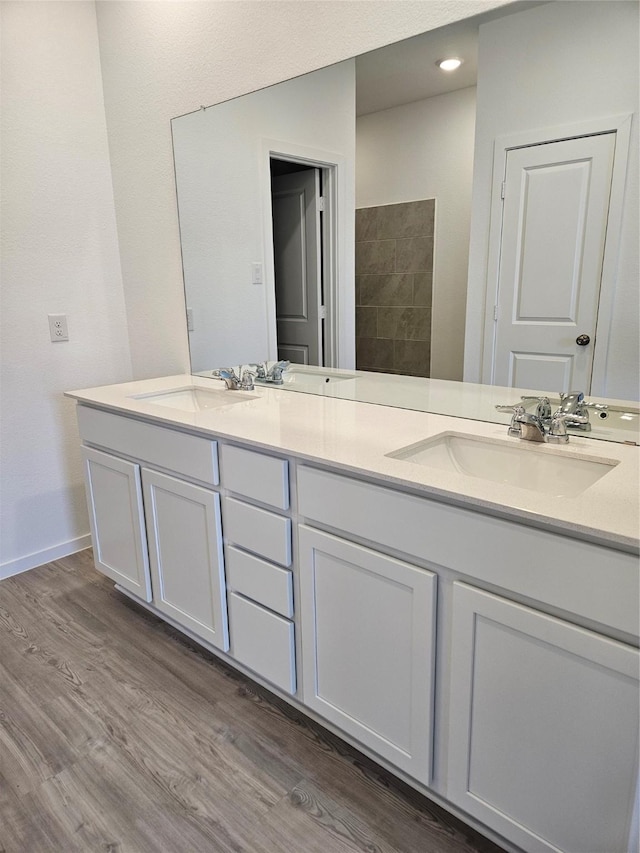 full bath featuring double vanity, a sink, wood finished floors, and baseboards
