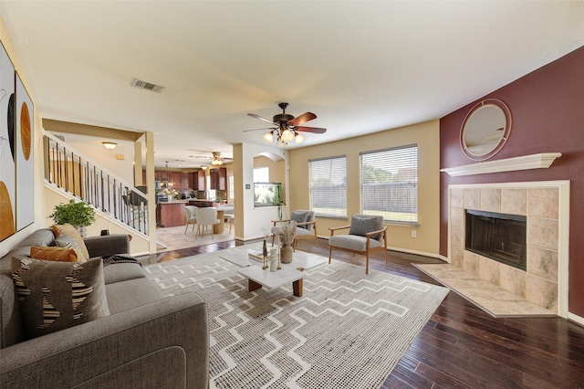 living room featuring hardwood / wood-style flooring, visible vents, a tiled fireplace, a ceiling fan, and stairs