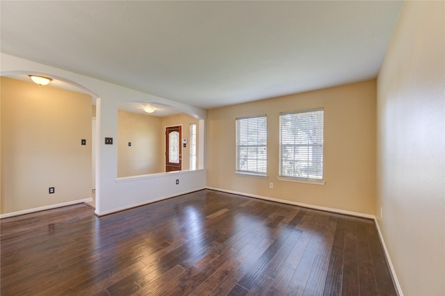 spare room featuring baseboards, arched walkways, and dark wood finished floors