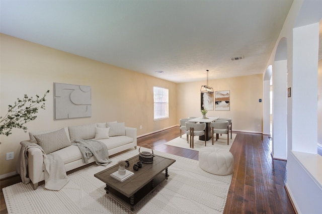 living room with visible vents, baseboards, dark wood finished floors, and arched walkways