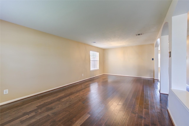 unfurnished room featuring arched walkways, visible vents, baseboards, and dark wood-type flooring